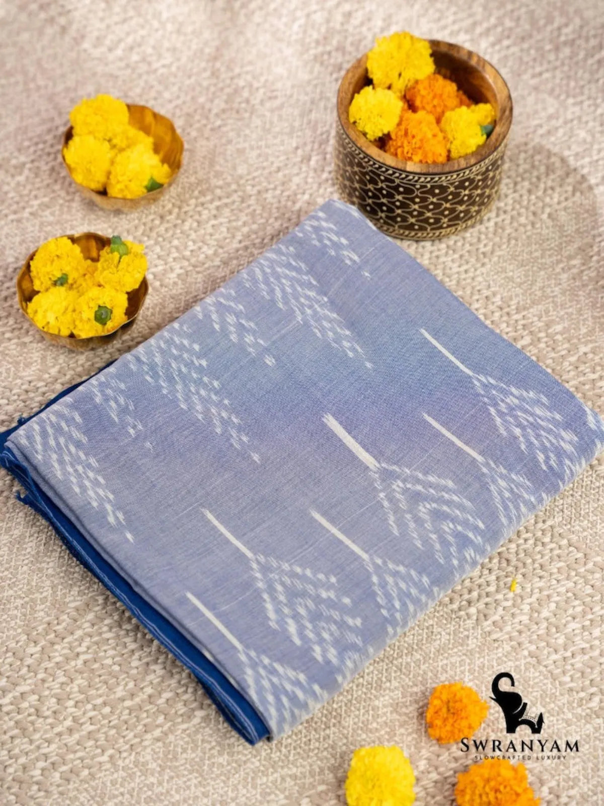Folded handwoven sky blue cotton ikat saree showing white tree leaf motifs on the body