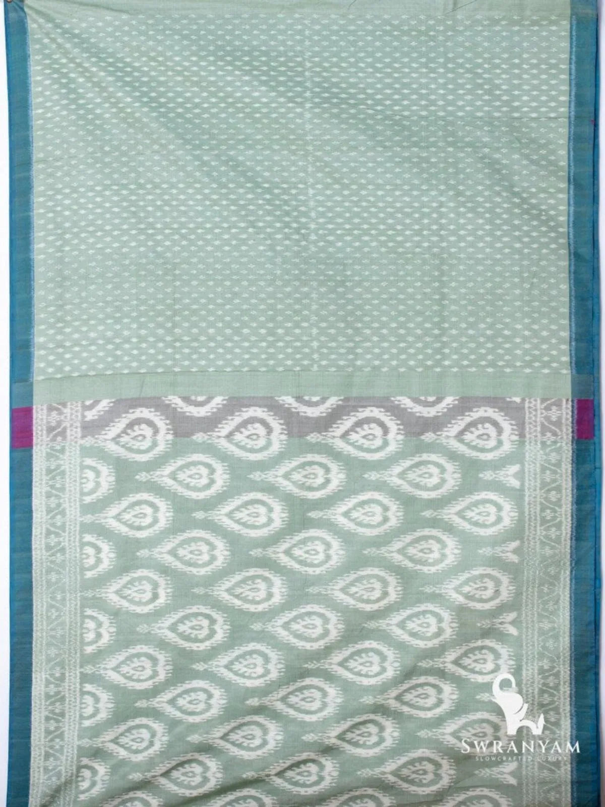 Flat lay of sage green ikat silk cotton saree showing butti body, heart motif pallu and teal border