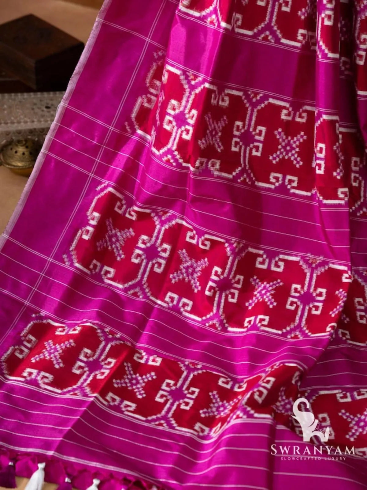 Magenta pallu with red double ikat motif panels, thin white pinstripes and white and purple tassels on Telia Rumal saree
