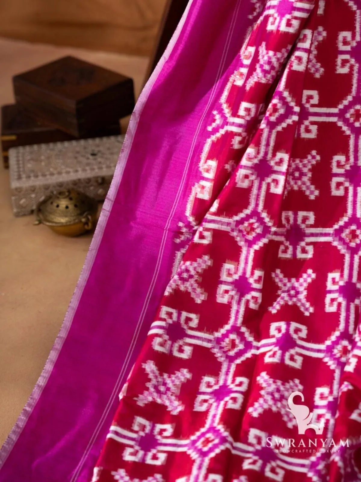 Plain magenta border with thin white pinstripes beside crimson red body with white and magenta double ikat motifs