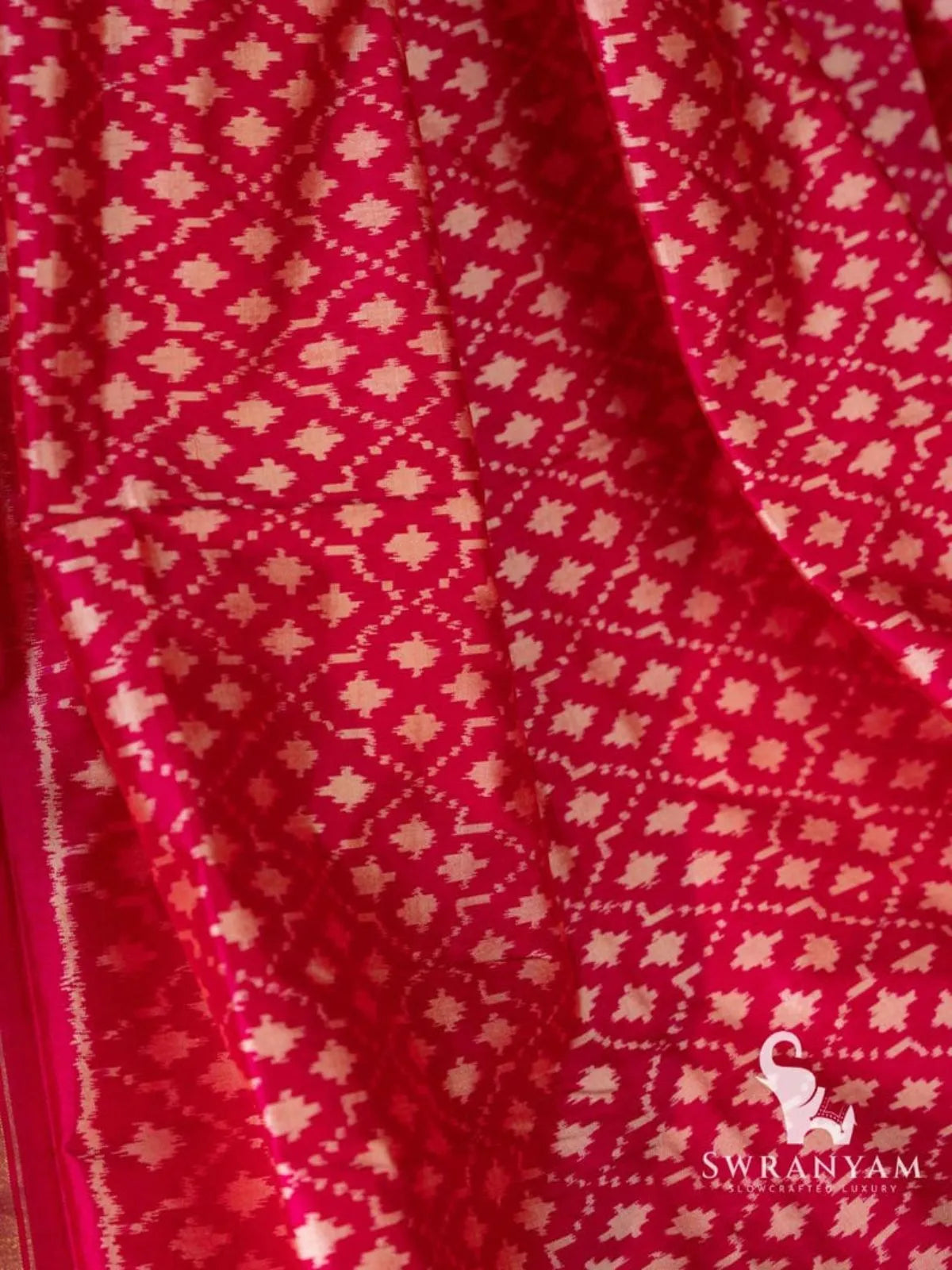 Pink silk saree folds showing rows of white geometric ikat motifs in diamond and star shapes