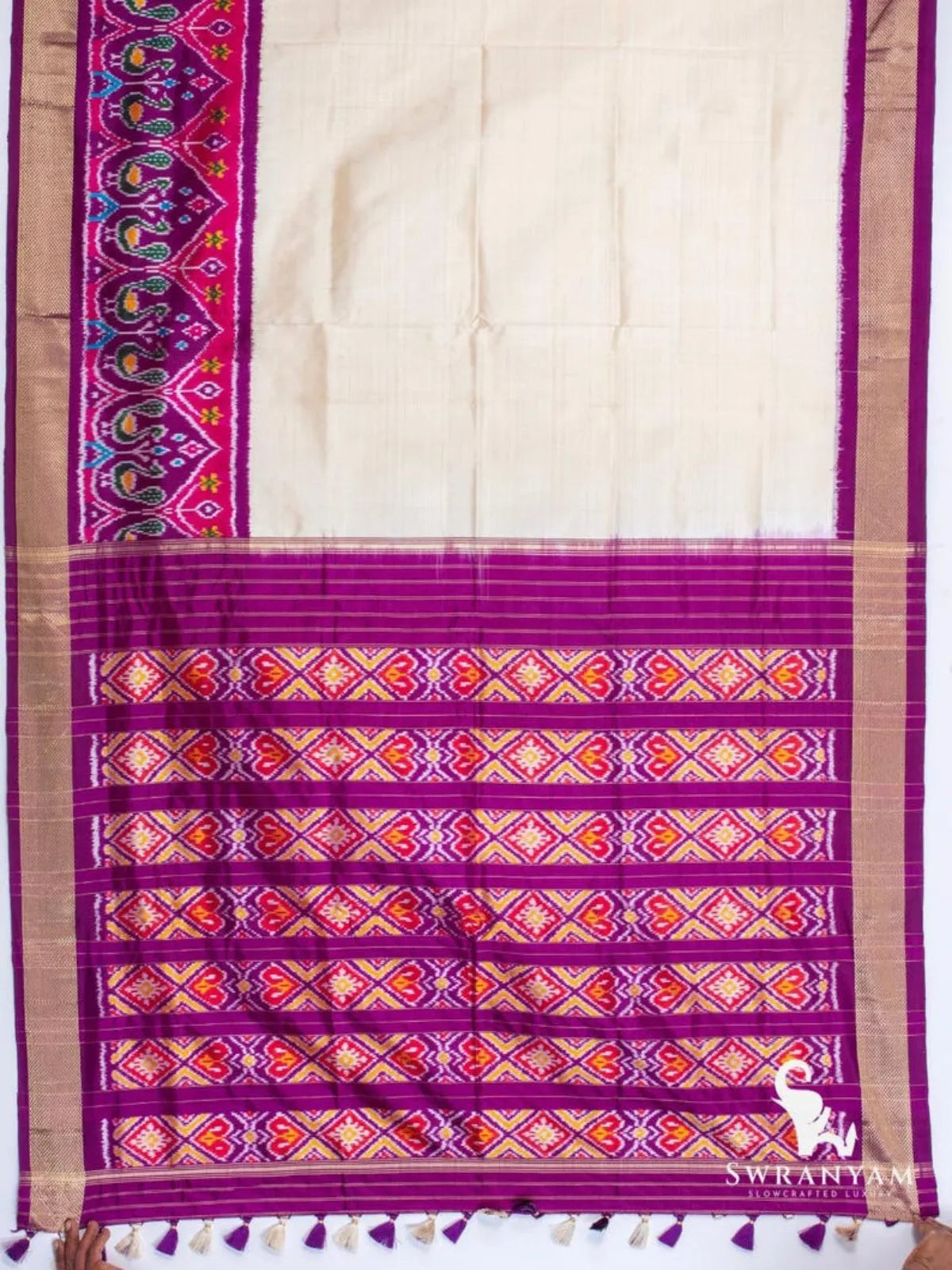 Full view of ivory silk saree with plain body, peacock ikat border and zari-striped purple ikat pallu