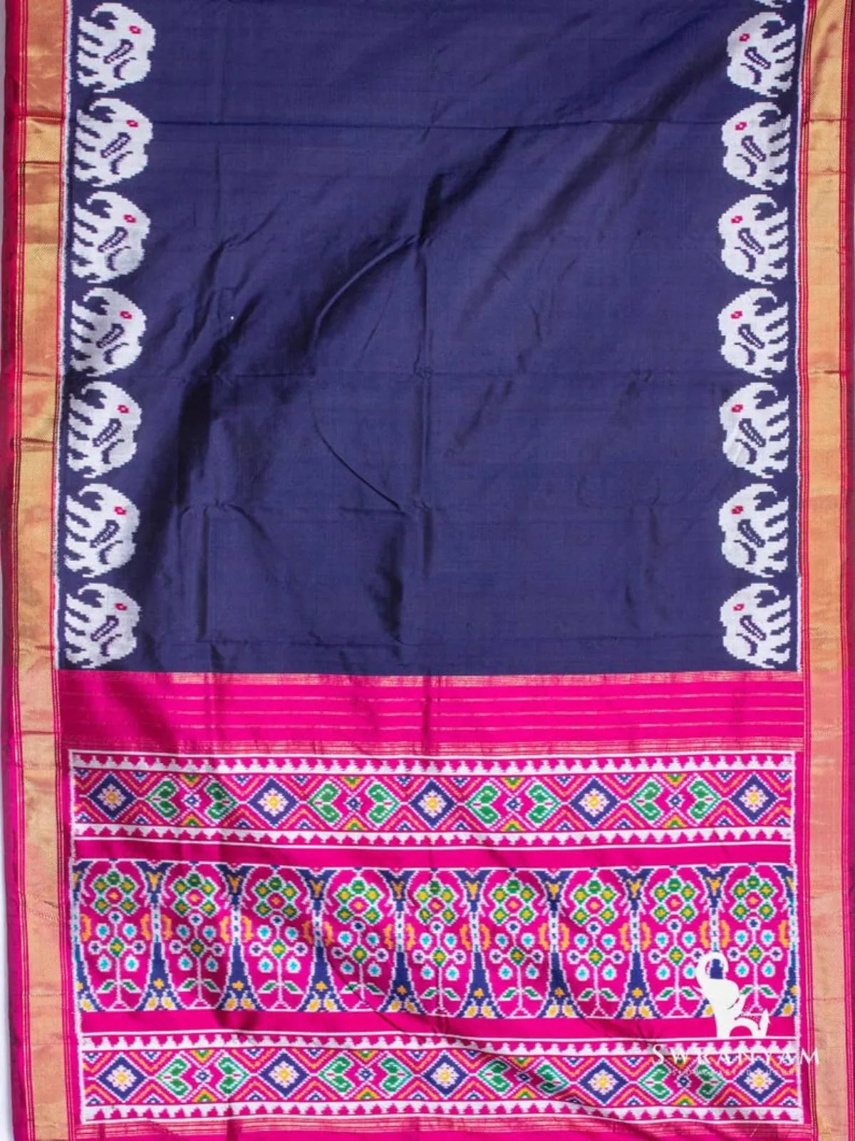 Navy blue ikat silk saree spread flat showing white elephant motif borders, gold zari edges and pink ikat pallu
