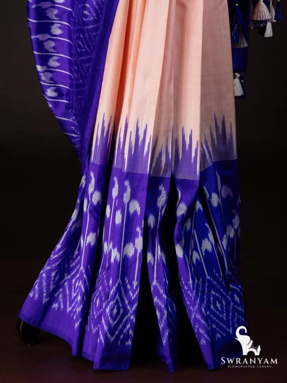 Peach tussar silk saree pleats with royal purple temple border and white ikat paisley and diamond hem pattern