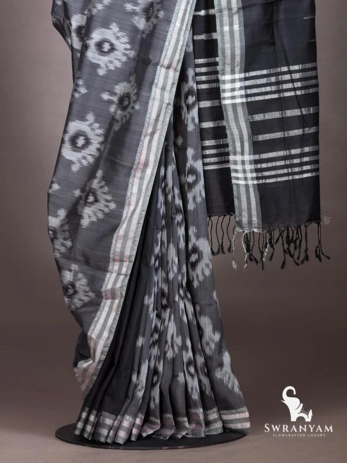 Charcoal grey weft ikat saree pleats with white ikat motifs and black pallu with silver stripes and black tassels