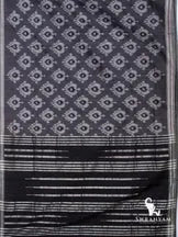 Charcoal grey Pochampally ikat cotton silk saree spread flat showing white ikat motifs and black pallu with silver stripes