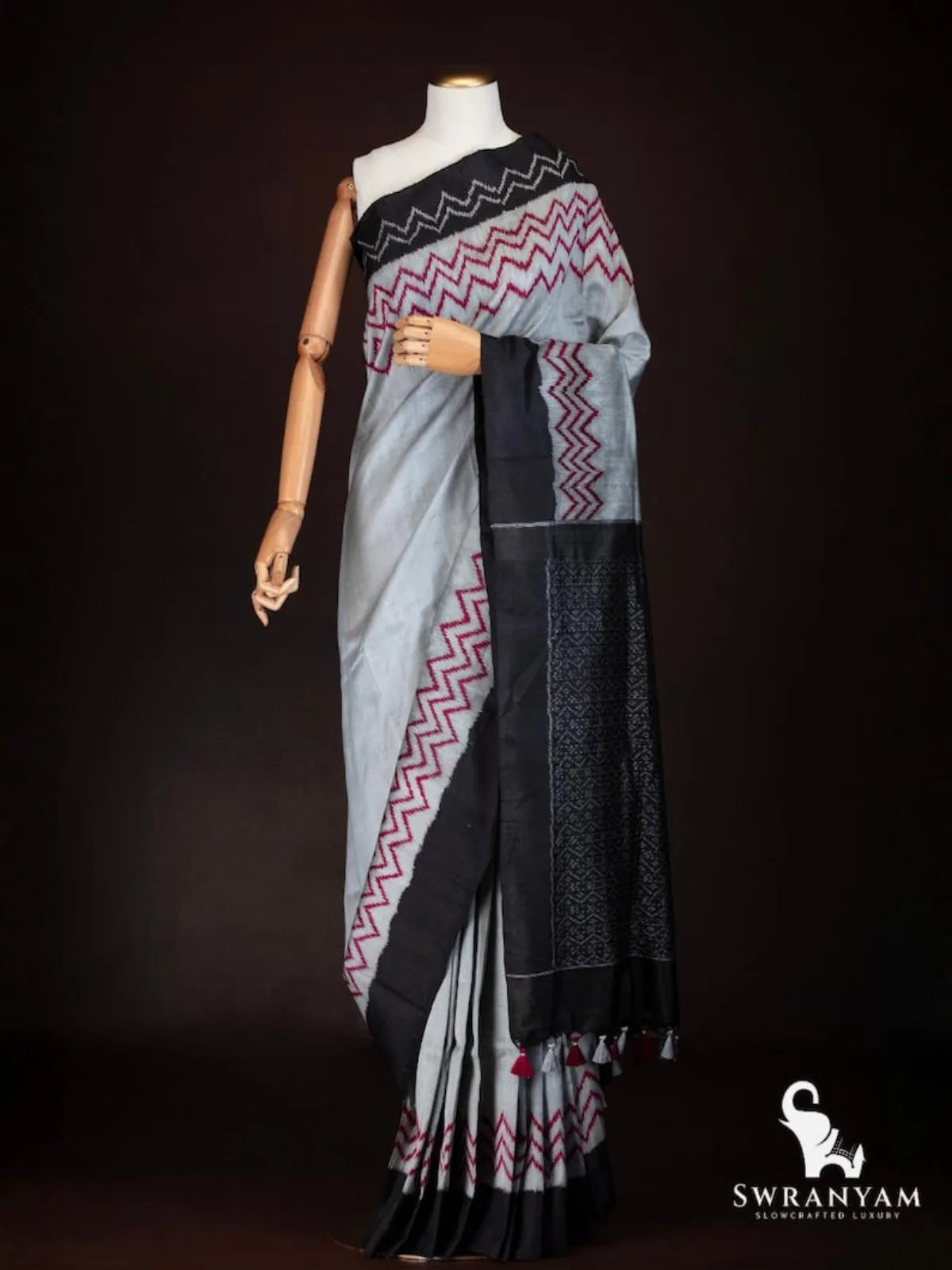 Charcoal grey Pochampally ikat tussar silk saree with red zigzag motifs and black border draped on mannequin