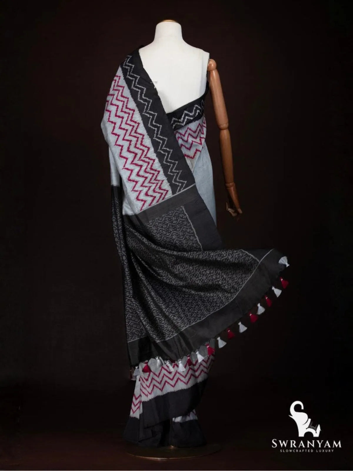 Back view of charcoal grey ikat tussar silk saree showing red zigzag body, black ikat pallu and tassels