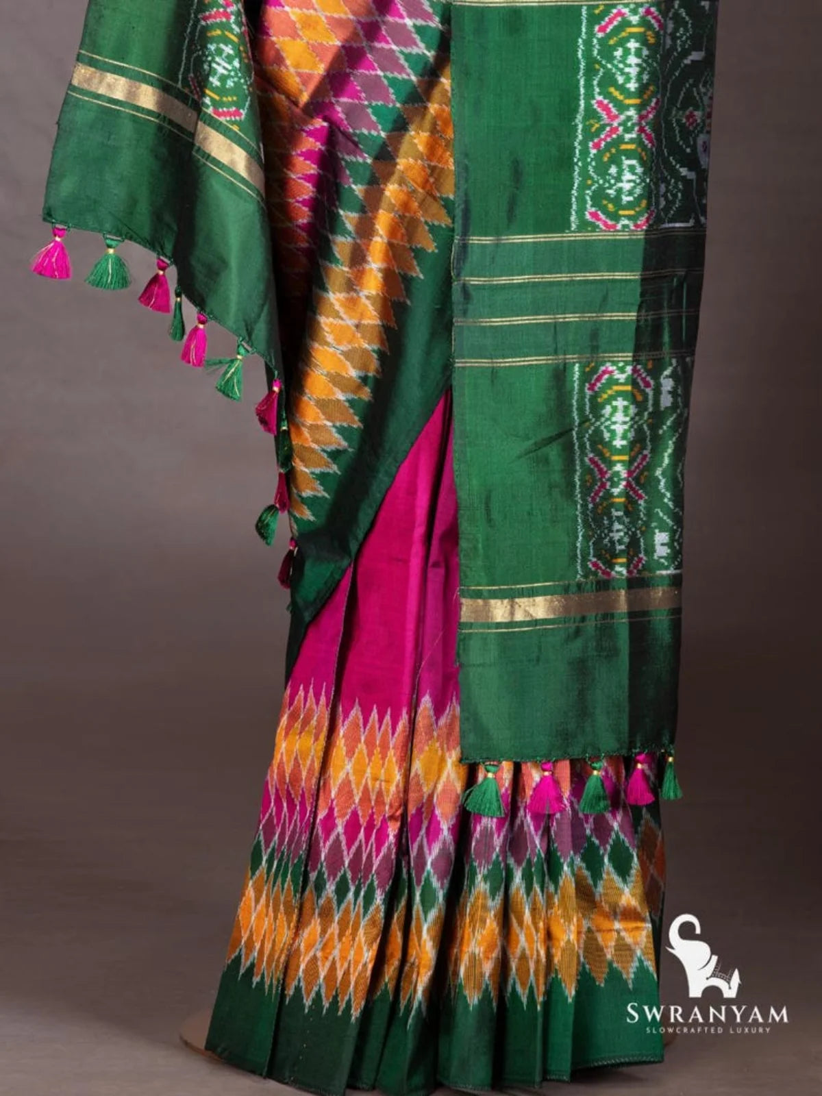 Wine purple ikat silk saree pleats with diamond ikat hem and emerald green pallu with zari stripes and pink green tassels