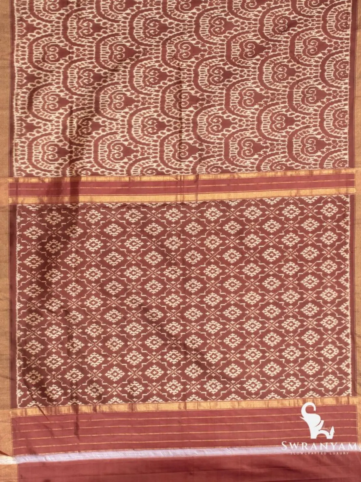 Flat lay of cocoa brown ikat silk saree showing swirl motif pallu and diamond ikat pattern with zari stripes