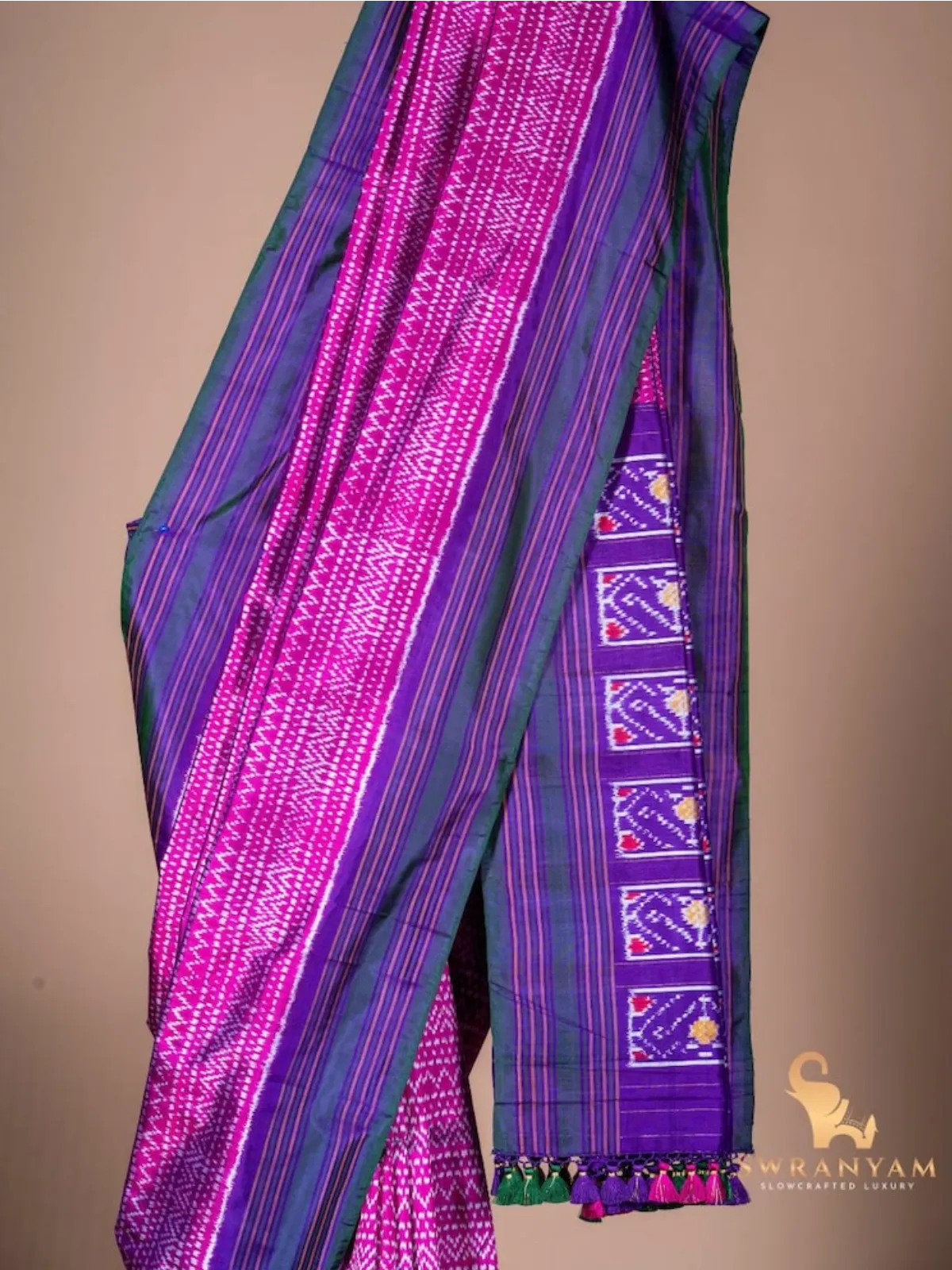 Close up of pink geometric ikat body and purple green border with ikat motif pallu and colourful tassels