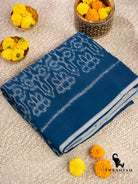 Folded indigo blue Pochampally ikat cotton saree with white floral ikat motifs and grey border beside marigold flowers
