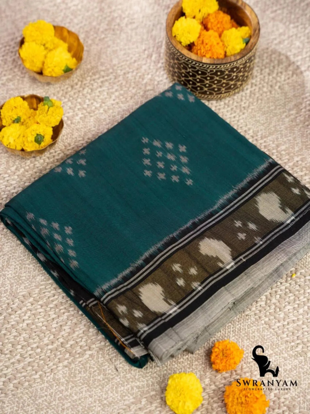 Folded emerald green Pochampally ikat cotton saree with black border and white paisley motifs beside marigold flowers