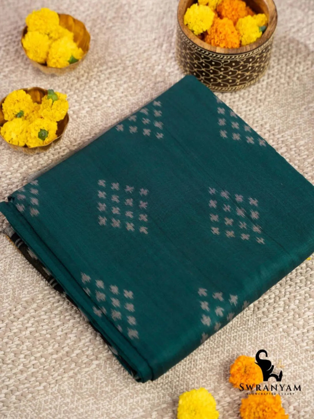 Folded handwoven emerald green cotton ikat saree showing white diamond butti motifs on the body