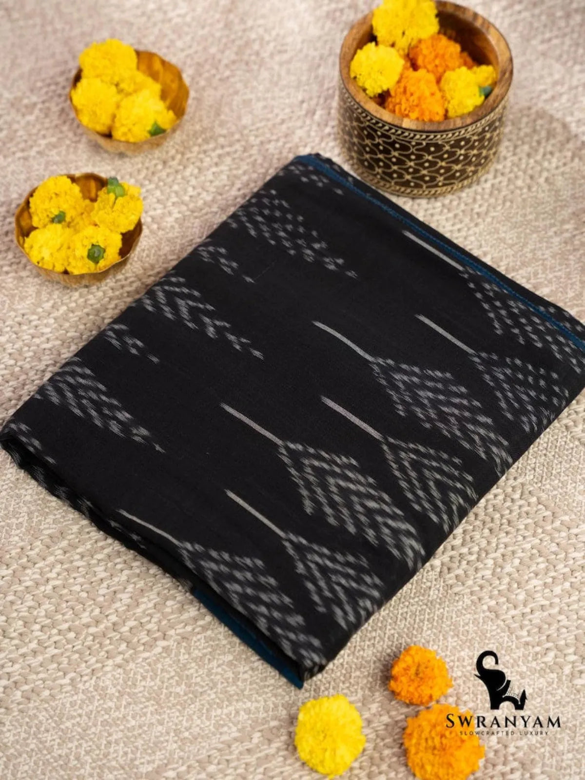 Folded handwoven black cotton ikat saree showing white tree leaf motifs on the body