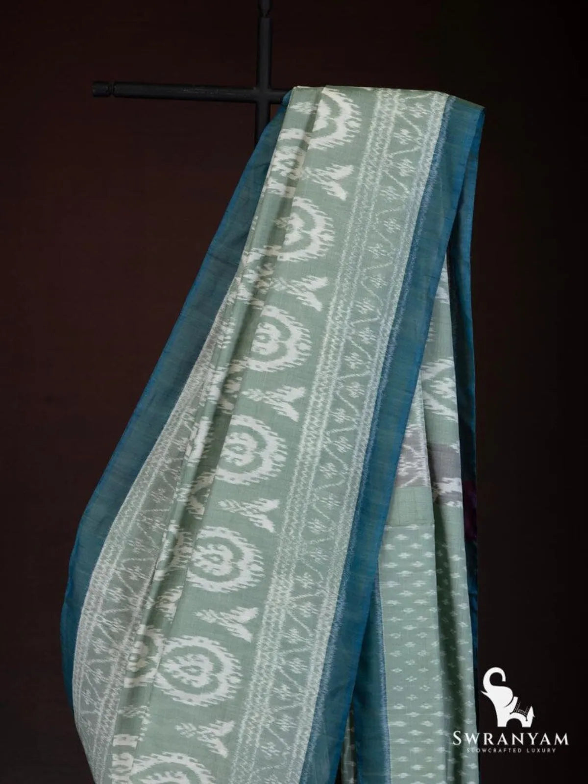 Close up of white paisley ikat motif border and teal edge on sage green weft ikat silk cotton saree