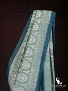 Close up of white paisley ikat motif border and teal edge on sage green weft ikat silk cotton saree
