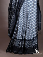 Pleats of grey checker ikat silk saree with black geometric ikat motif border at the hem