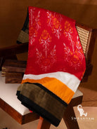 Red Pochampally ikat silk saree with yellow and white panels and black golden zari border draped on a cane chair