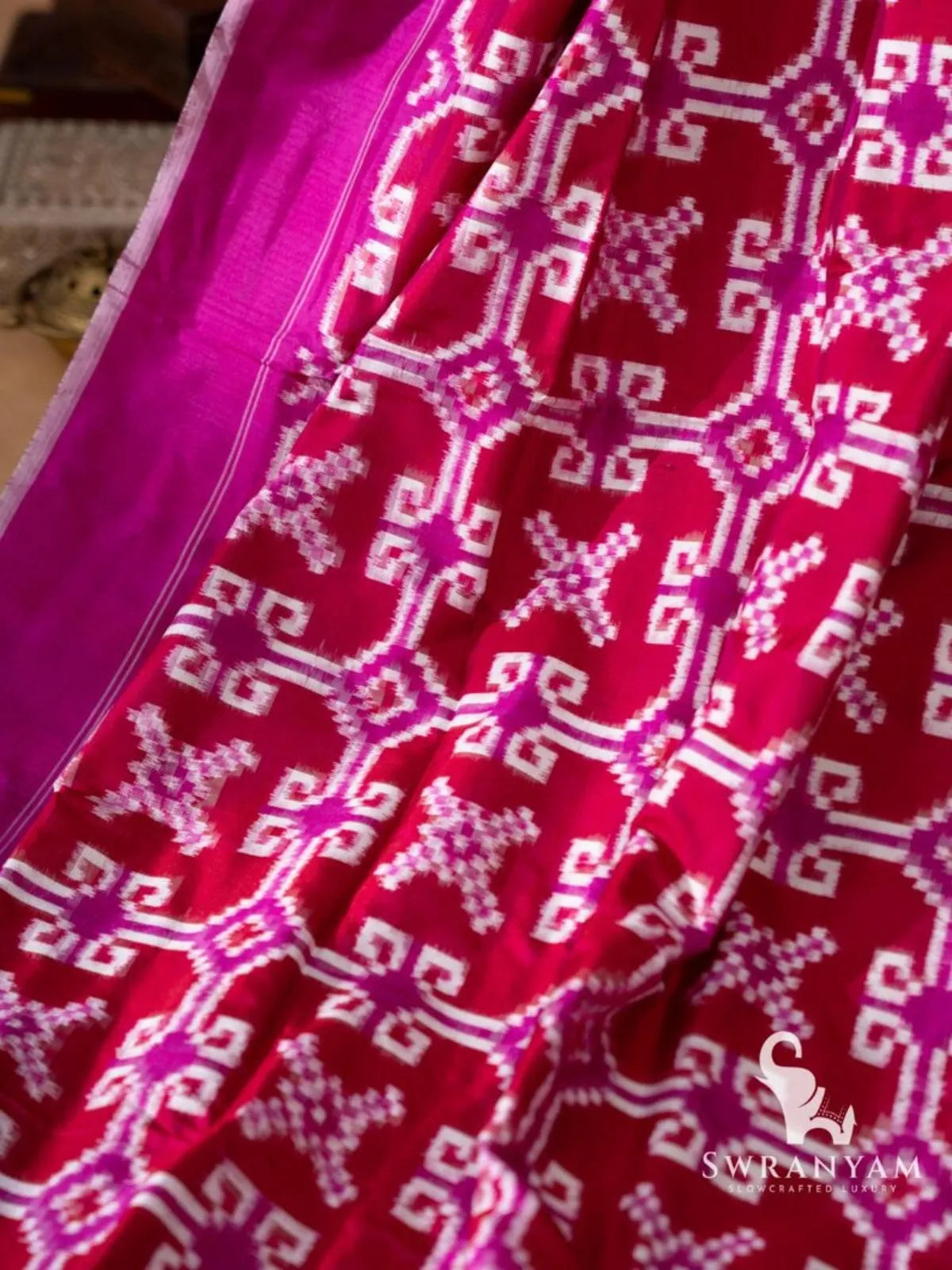 Close-up of white and magenta geometric double ikat motifs on crimson red silk saree beside magenta border