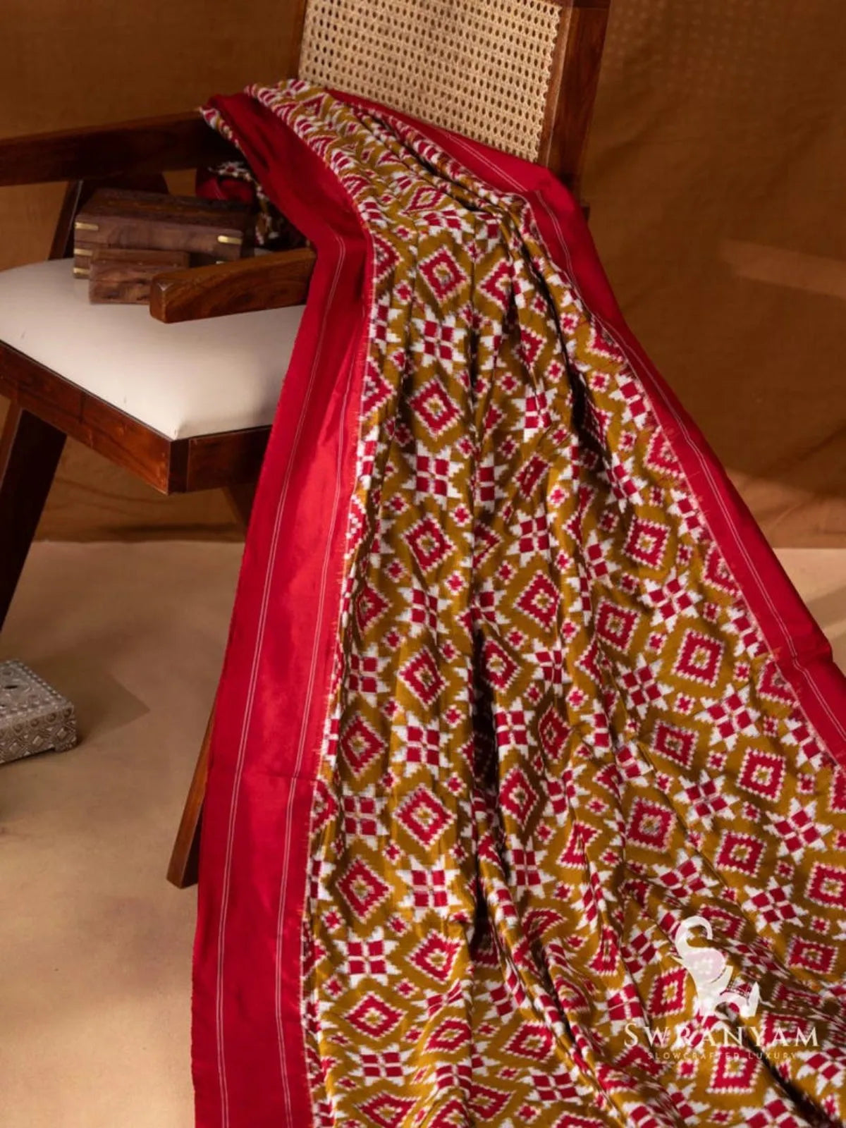 Olive green double ikat silk saree body with red and white diamond and star motifs and plain red border draped on chair