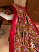 Olive green double ikat silk saree body with red and white diamond and star motifs and plain red border draped on chair