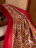 Olive green double ikat silk saree folds on chair showing red and white diamond ikat motifs and red border edge