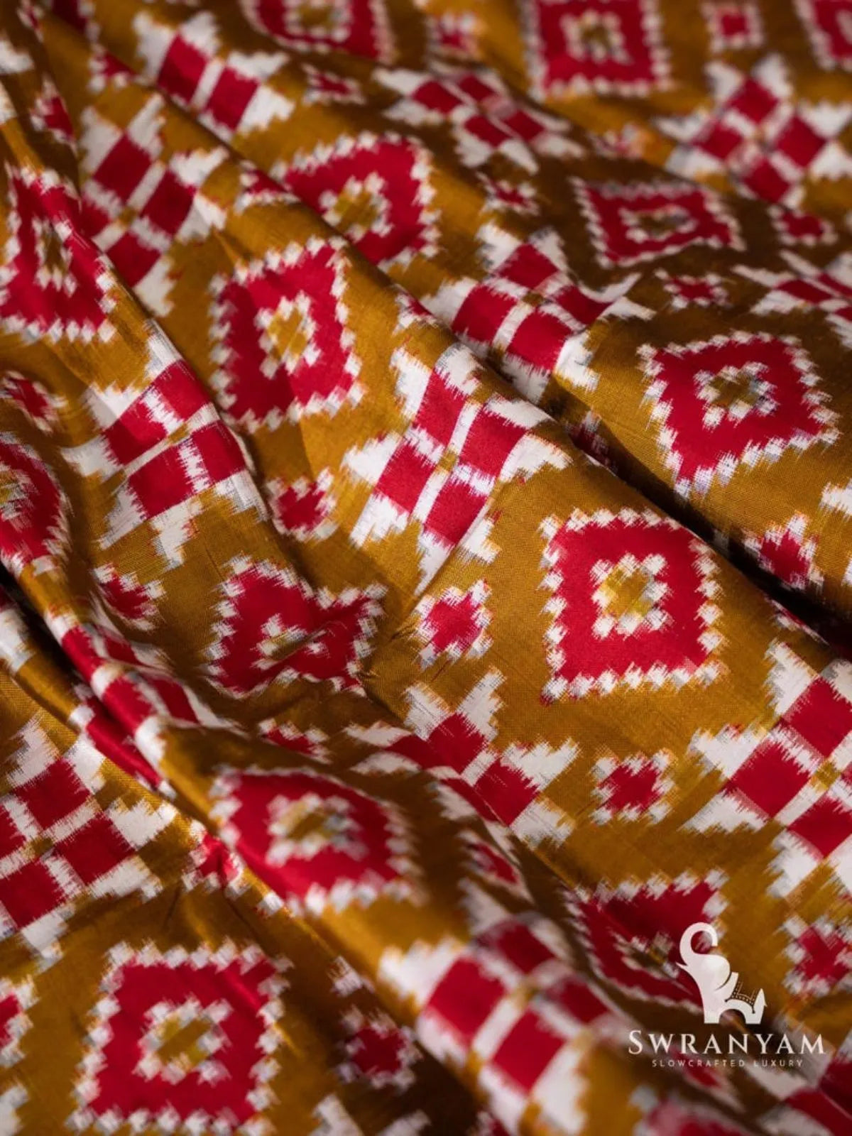 Close-up of red and white diamond and checker ikat motifs on olive green Pochampally double ikat silk fabric