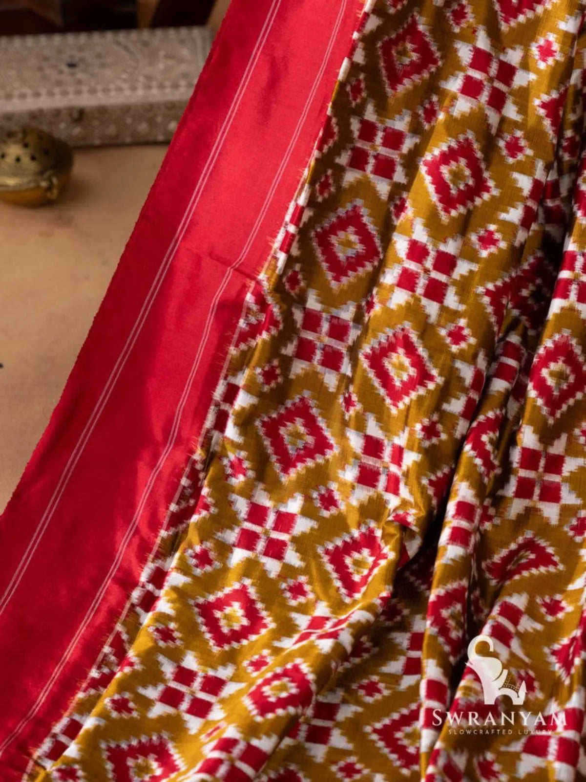 Close-up of plain red border with thin white pinstripes beside olive green double ikat body with red diamond motifs