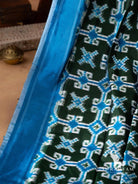 Blue border with white pinstripes beside bottle green body with blue and white double ikat motifs on silk saree
