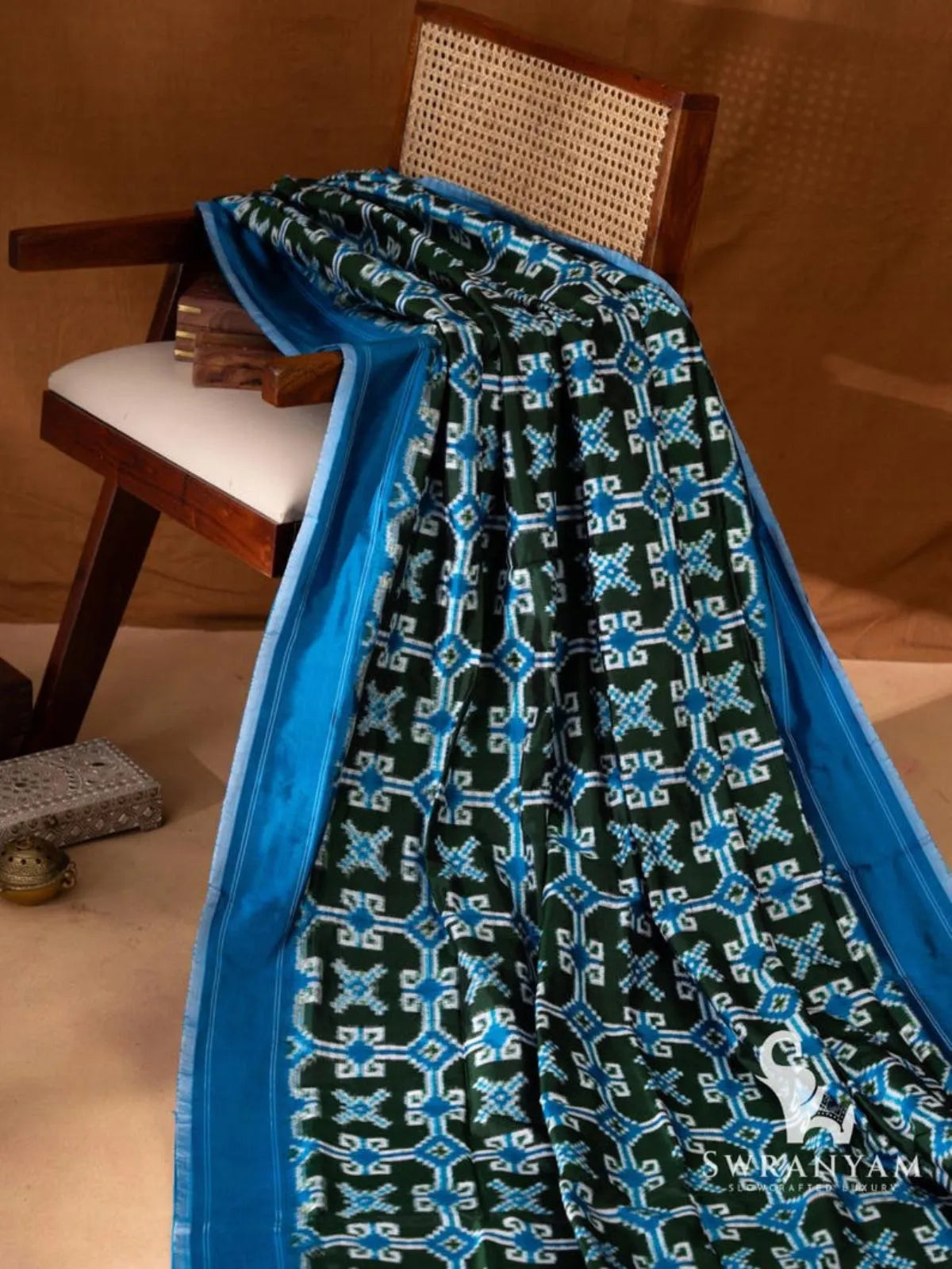 Bottle green double ikat silk saree body with blue and white geometric ikat motifs and blue pinstriped border on chair