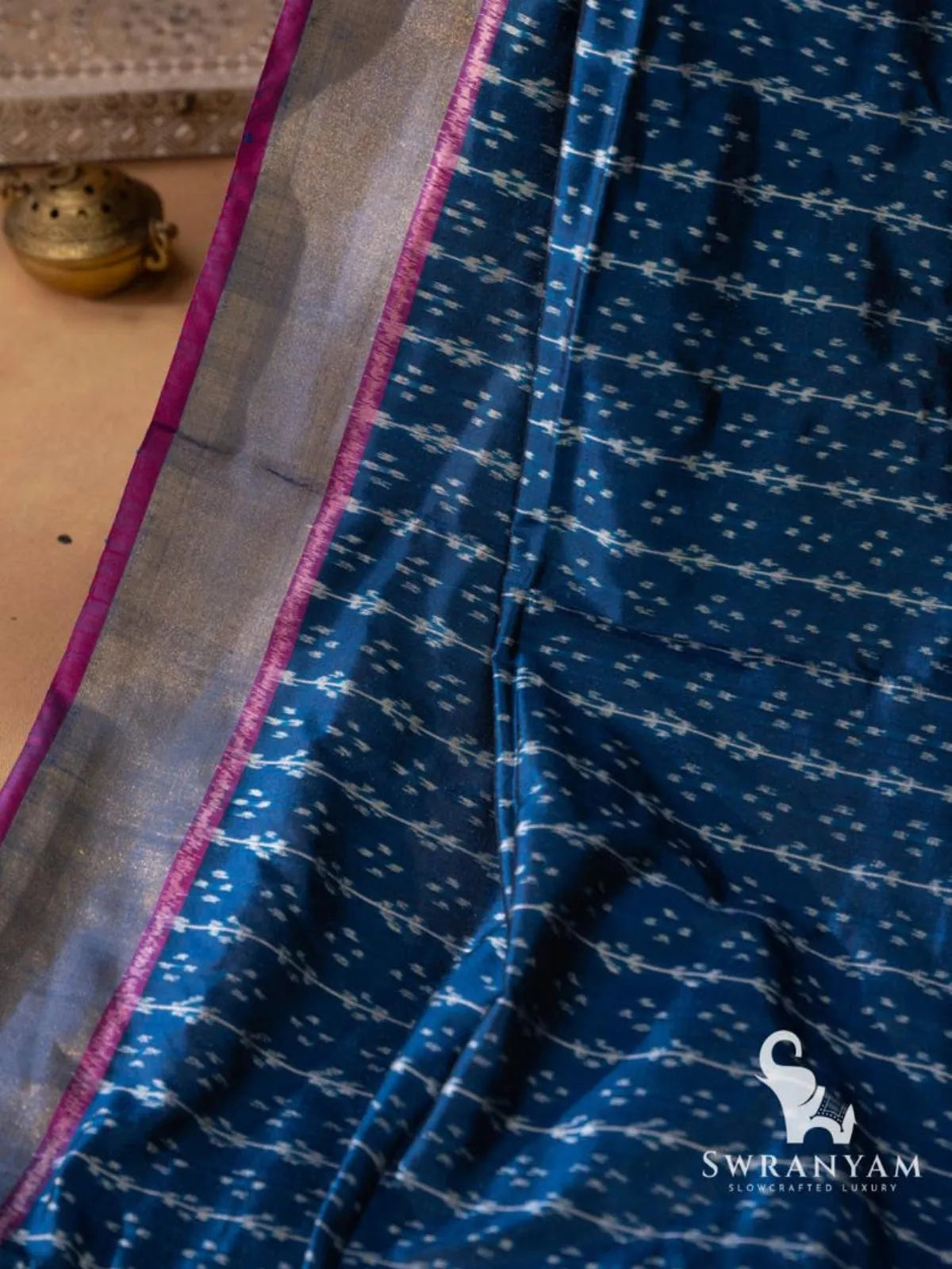 Close-up of silver gold zari border with pink edging beside white ikat motifs on indigo blue silk saree
