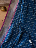 Close-up of silver gold zari border with pink edging beside white ikat motifs on indigo blue silk saree