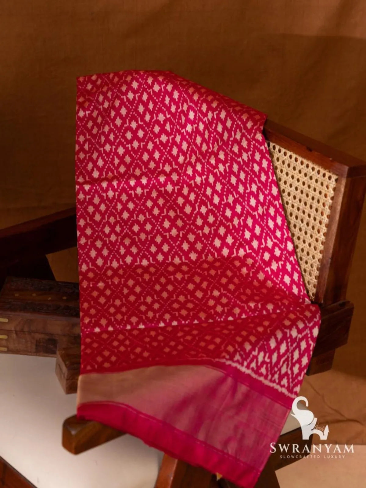 Pink Pochampally ikat silk saree with white geometric ikat motifs and gold zari border folded on wooden chair