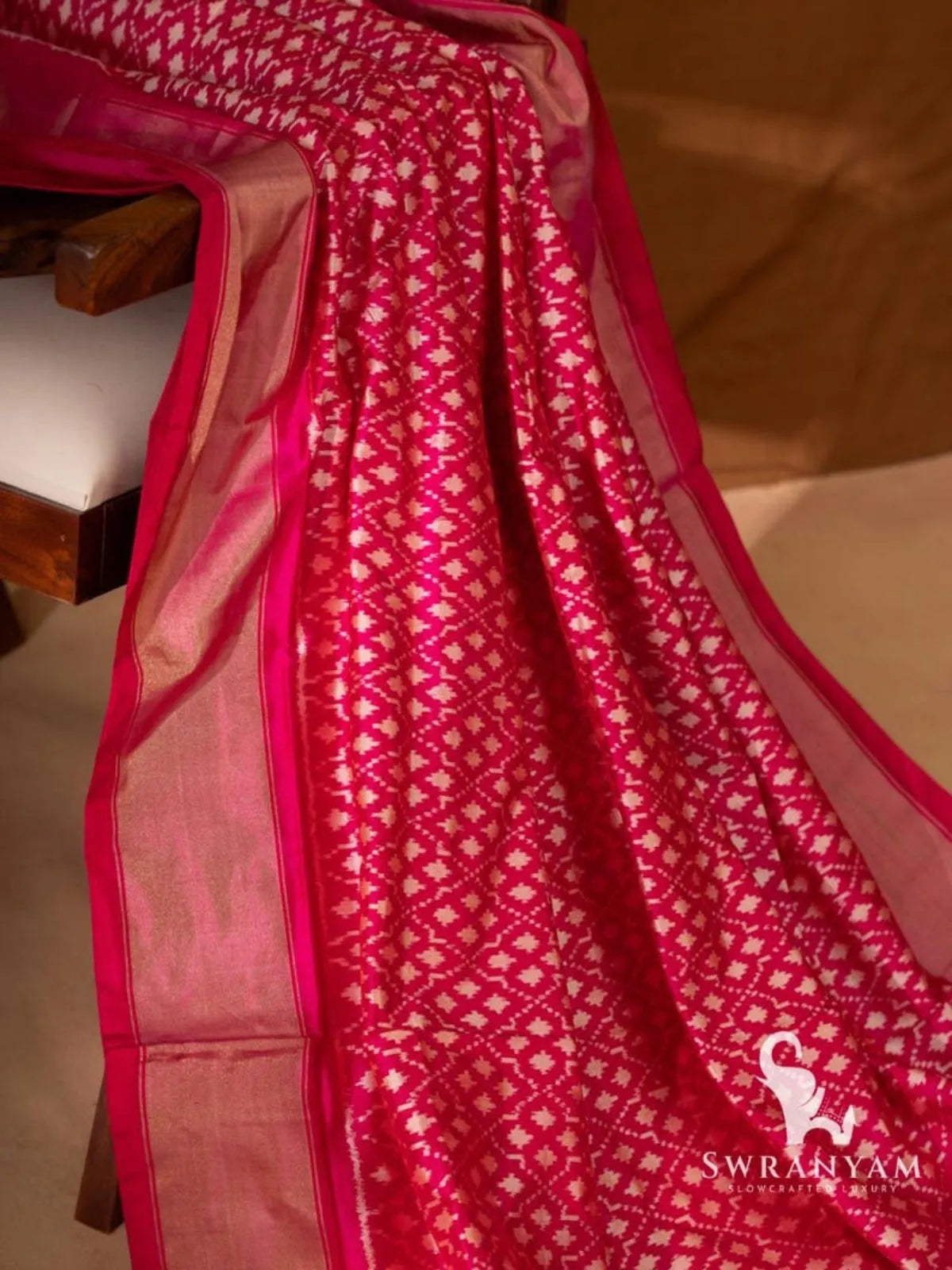 Close view of pink Pochampally ikat silk saree with white geometric motifs and gold zari border on a chair