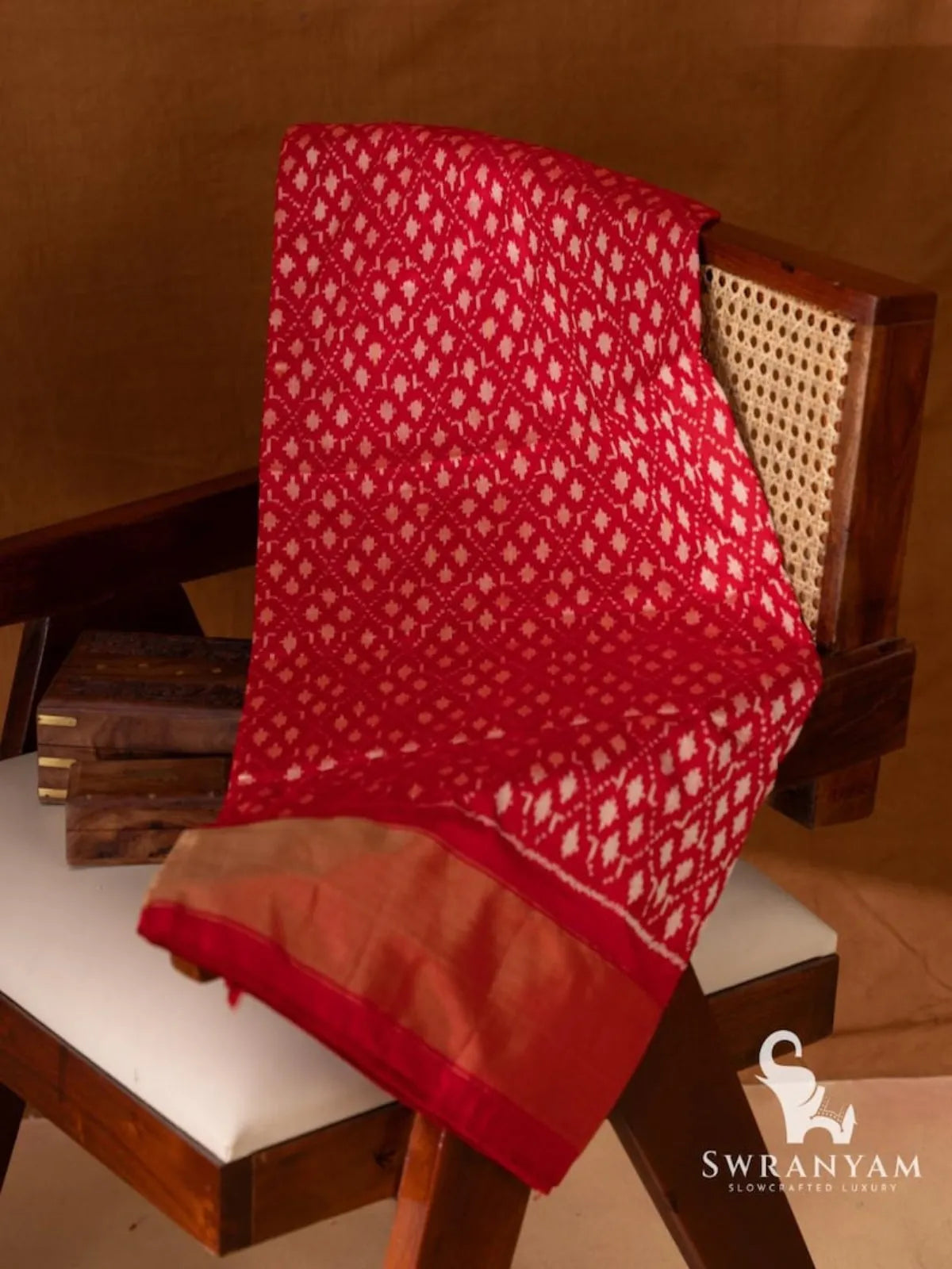 Red Pochampally single ikat silk saree with white geometric ikat motifs and gold zari border folded on wooden chair
