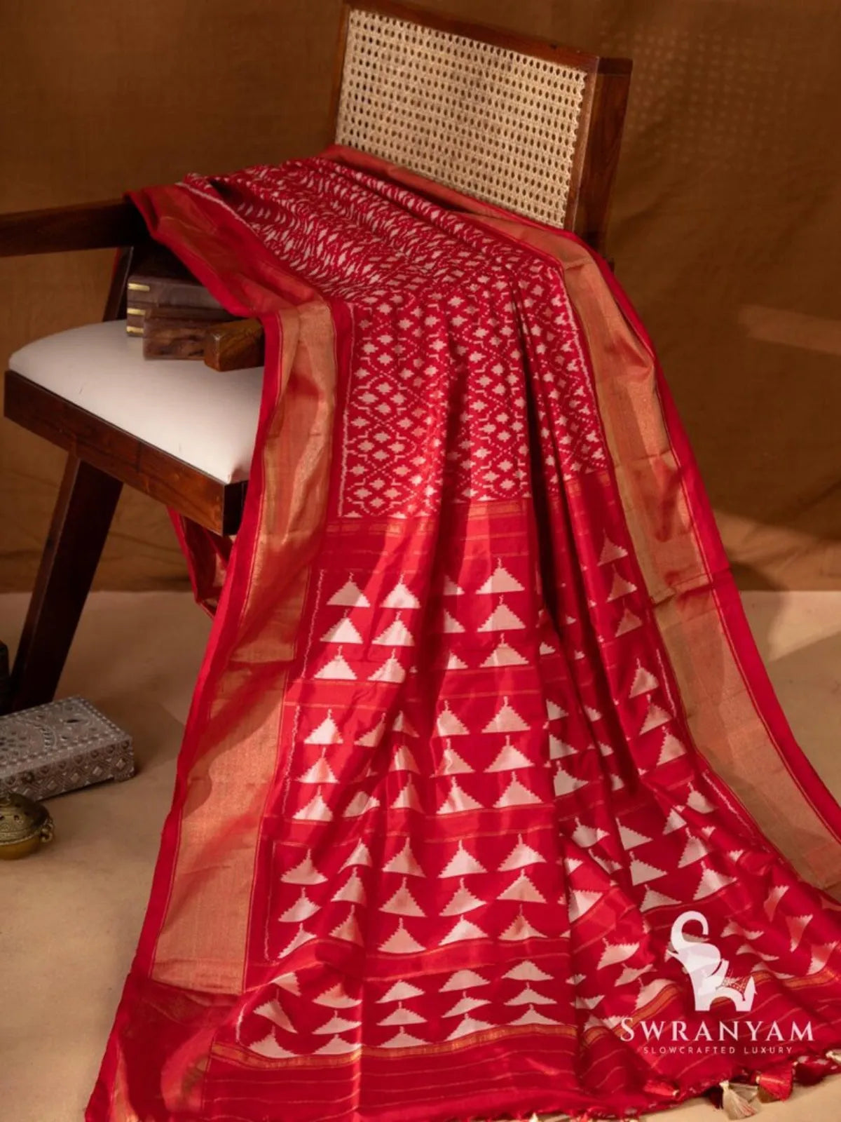 Red Pochampally ikat silk saree with gold zari borders and pallu with white temple motifs and tassels draped on chair