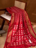 Red Pochampally ikat silk saree with gold zari borders and pallu with white temple motifs and tassels draped on chair