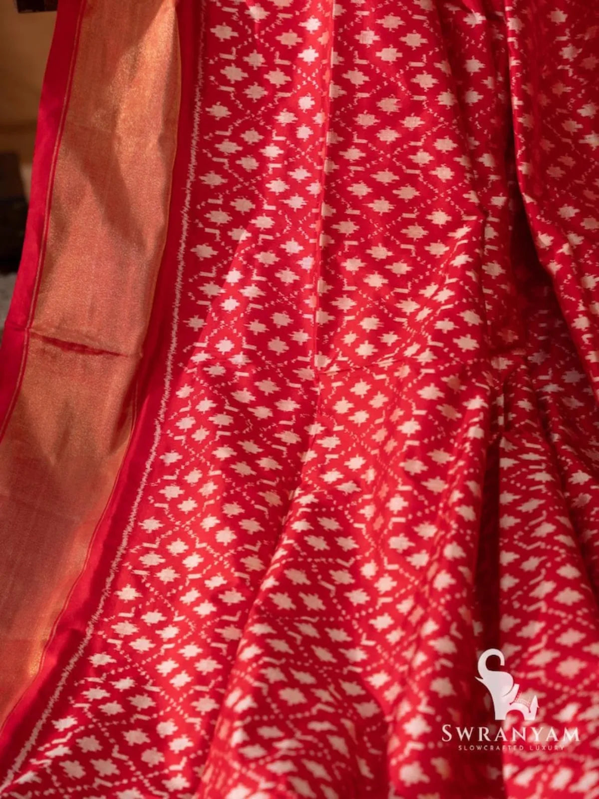 Close-up of red silk saree body with white geometric single ikat motifs beside wide gold zari border