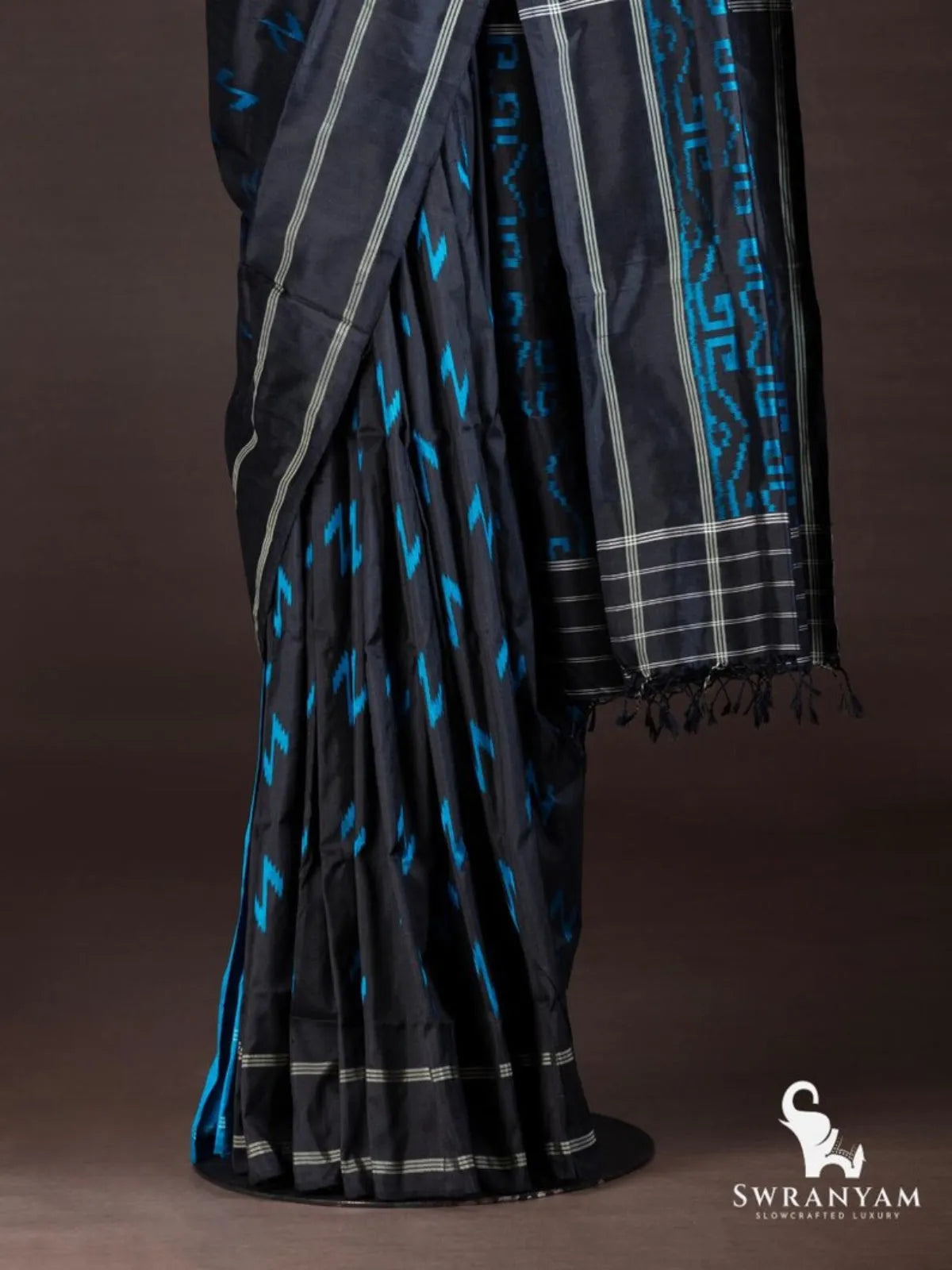 Black ikat silk saree pleats with blue zigzag motifs and silver striped hem, pallu with blue maze ikat pattern and fringe