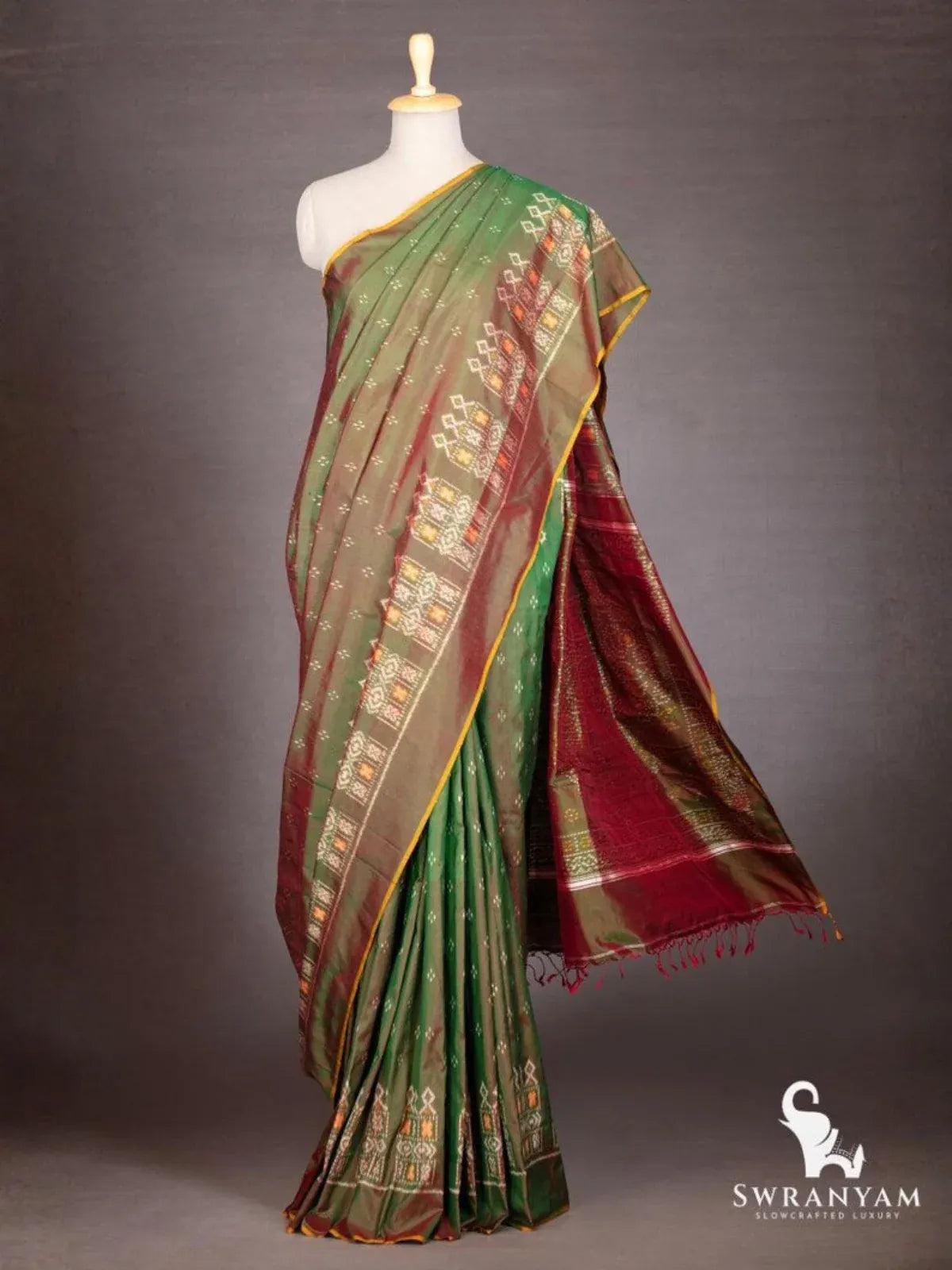 Bottle green Pochampally ikat silk saree with maroon pallu and tassels flowing, shown on mannequin