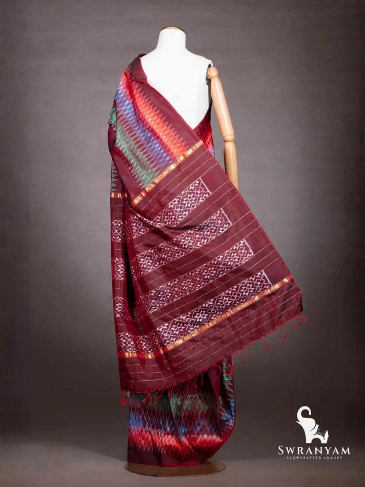 Back view of maroon ikat silk saree showing pallu with white ikat motif panels, gold zari stripes and red tassels