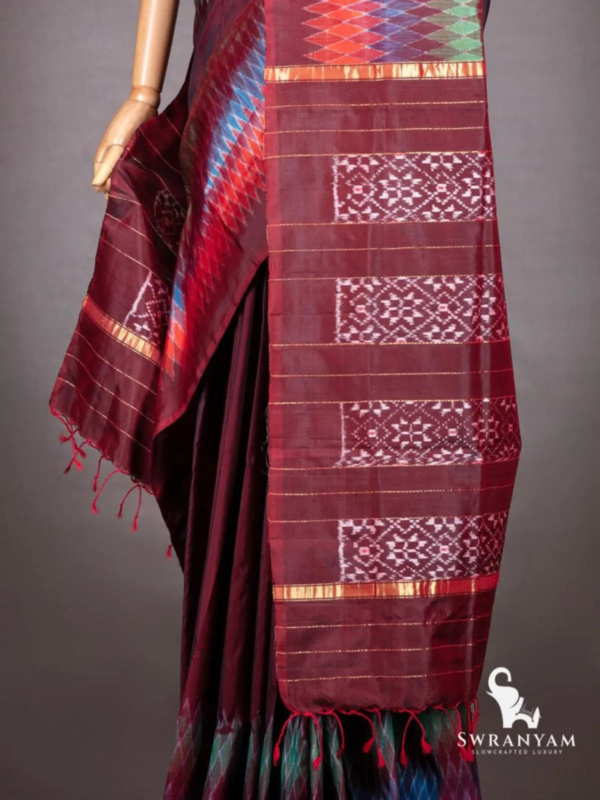 Close-up of maroon pallu with white ikat star motif panels, gold zari bands and twisted red tassels