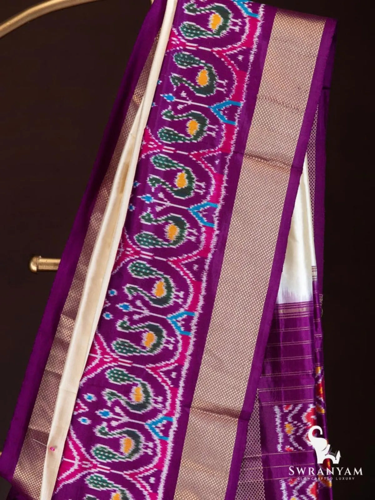 Close-up of royal purple and pink ikat border with green and yellow peacock motifs and gold zari band on ivory silk saree