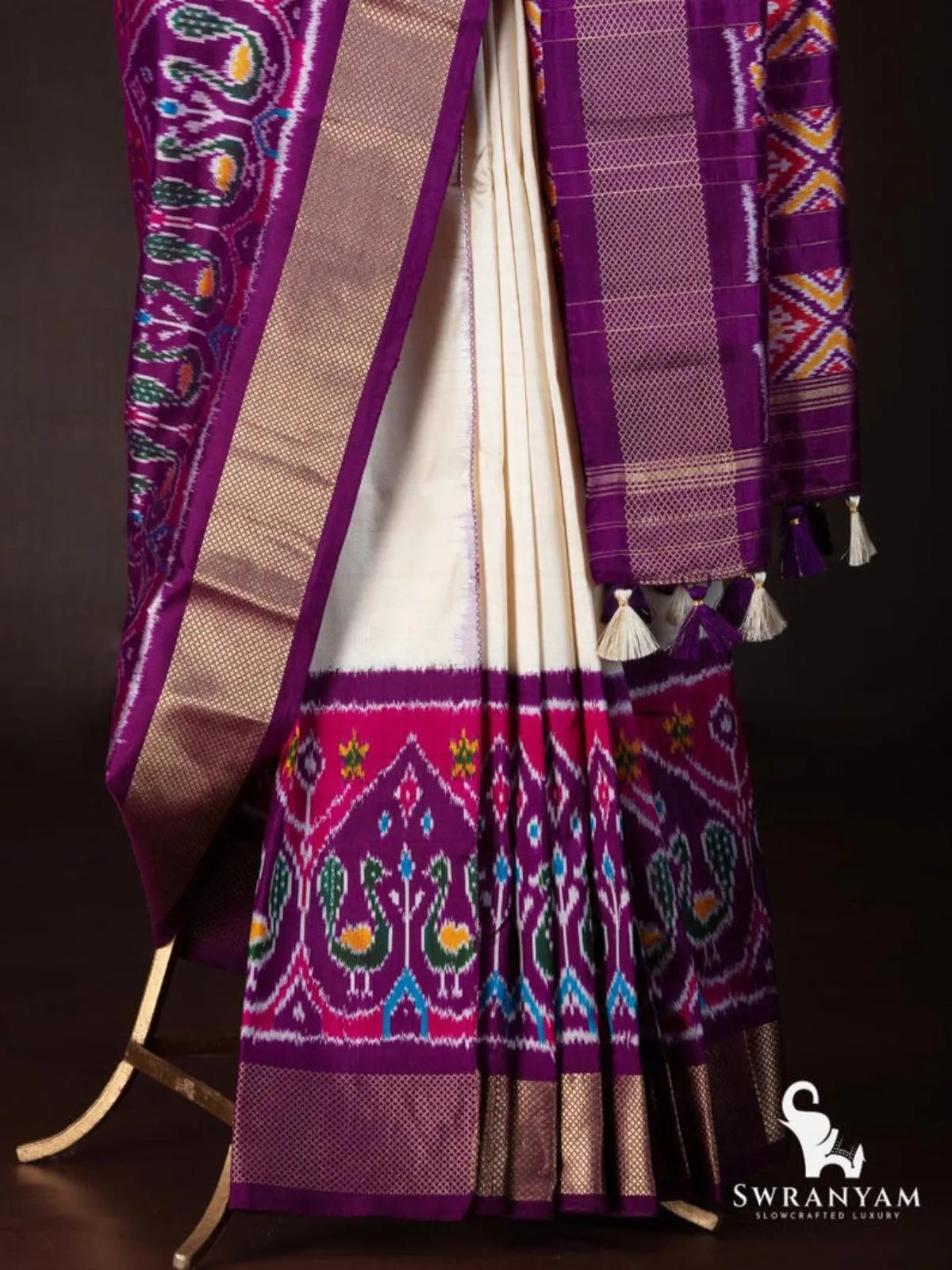 Ivory silk saree pleats with royal purple and pink peacock ikat hem border, gold zari edge and tasselled purple pallu