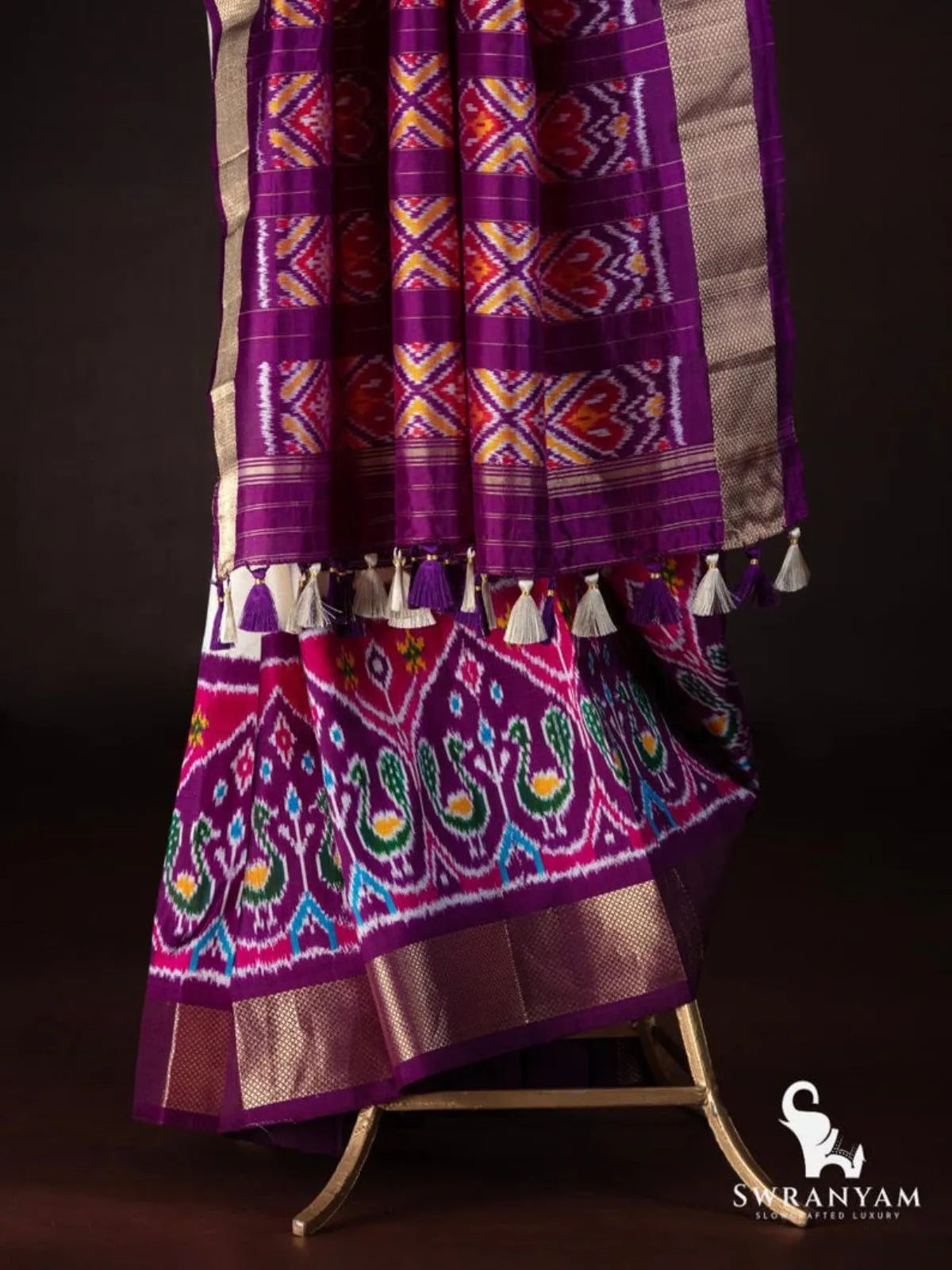 Purple pallu with red and yellow ikat panels and cream tassels above peacock ikat hem border on ivory saree