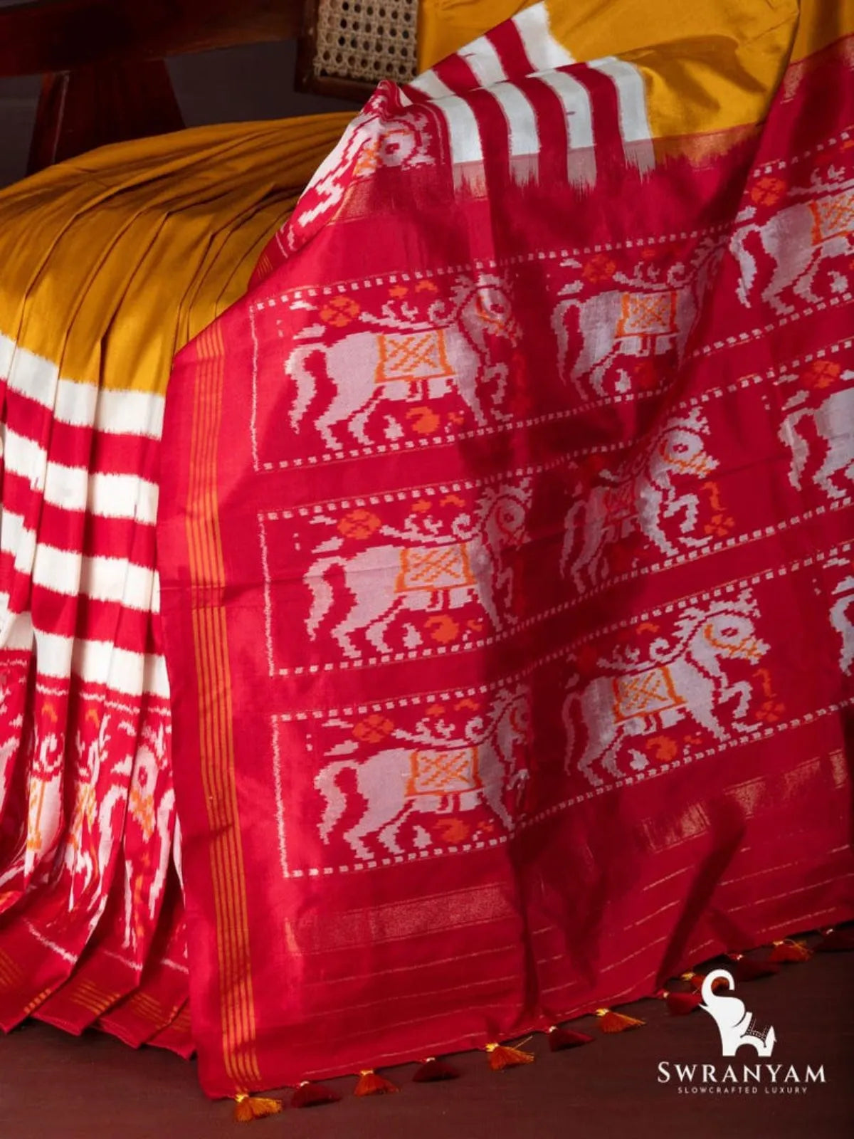 Close-up of crimson red pallu with white and orange horse ikat motifs, zari stripes and tassels on mustard yellow saree