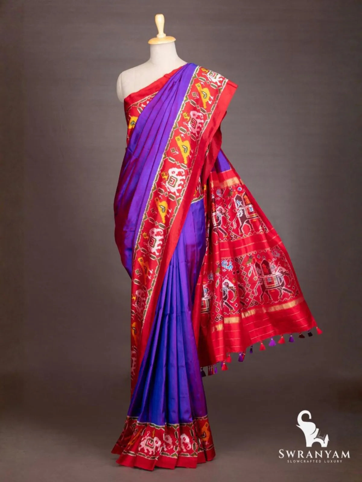 Royal purple ikat silk saree draped on mannequin with red pallu showing elephant procession and bird ikat motifs