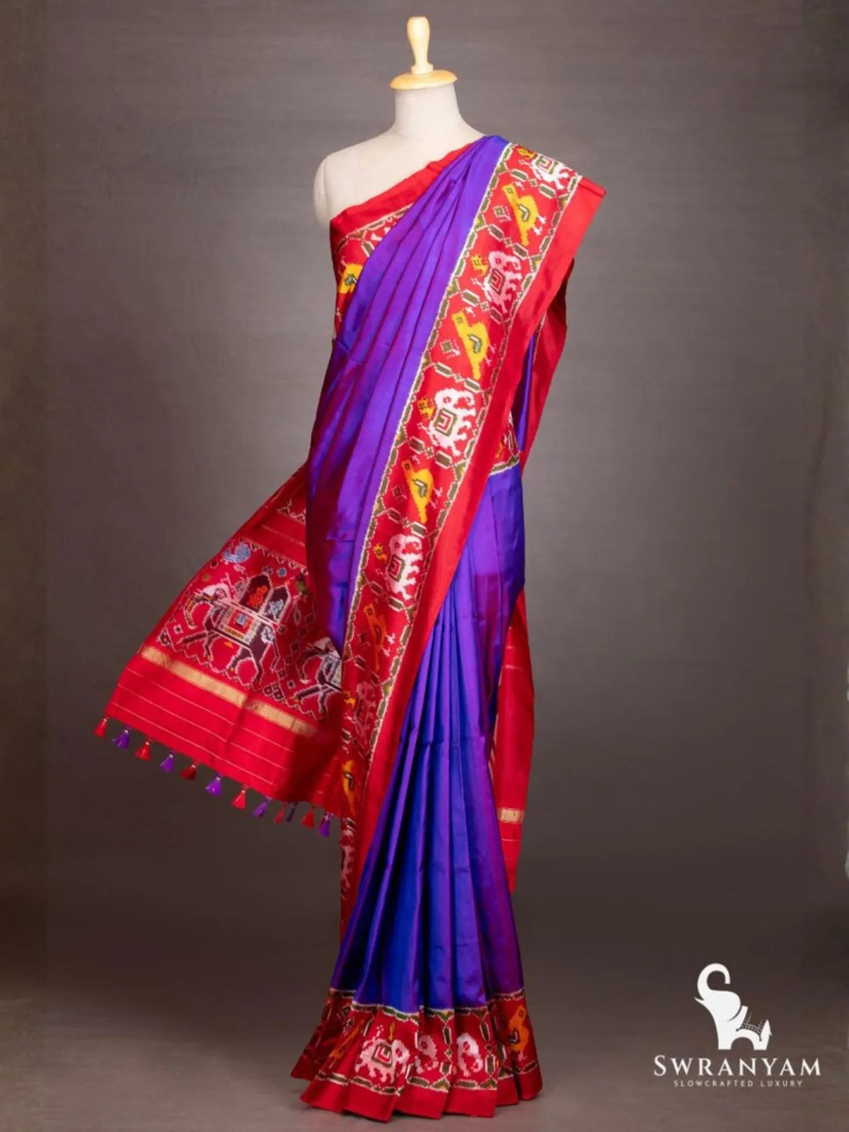 Royal purple ikat silk saree with red border and flowing red pallu with elephant procession motifs and tassels
