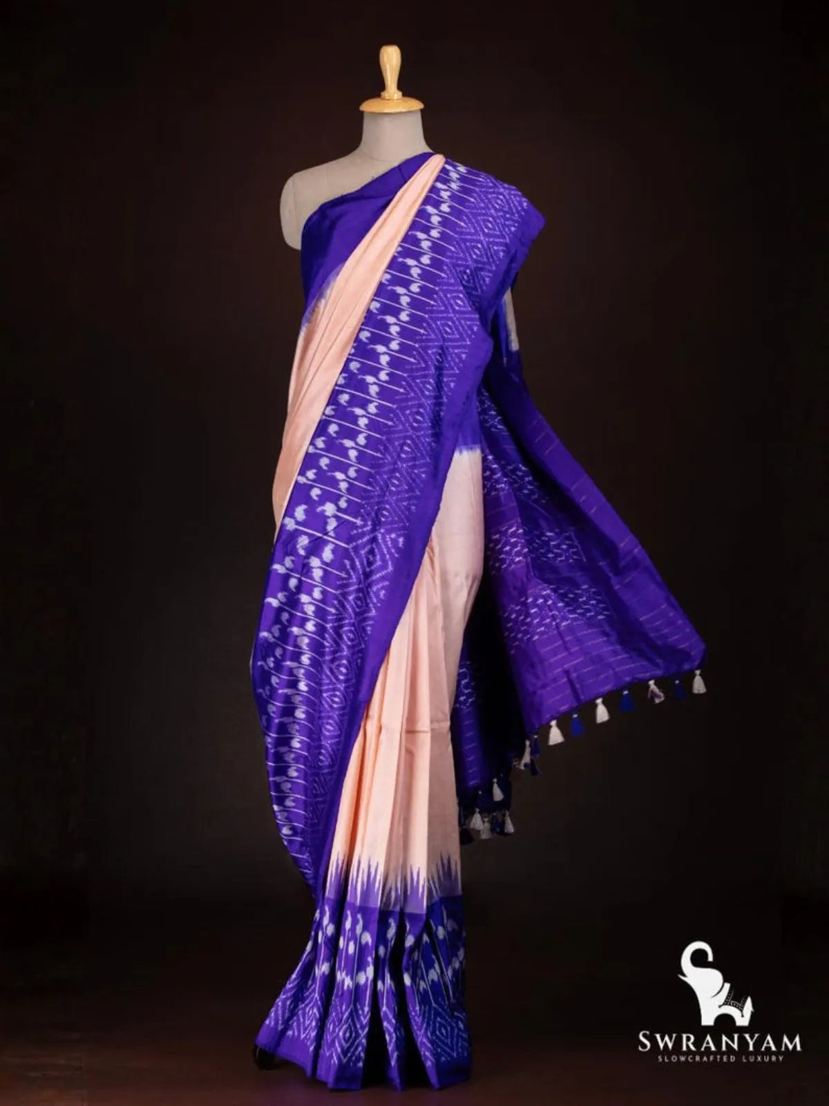 Royal purple and peach Pochampally tussar silk saree with white ikat motifs and purple pallu with tassels on mannequin